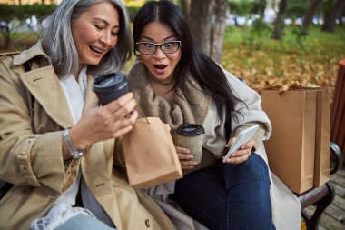 Küçük alışveriş çantasının içine bakan neşeli bayan arkadaşlar.