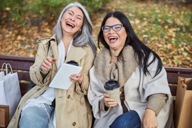 İki neşeli kadın bankta oturuyor ve gülüyor.