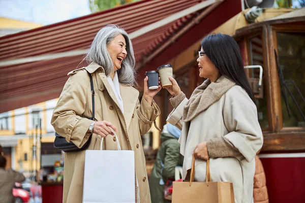 Neşeli bayan arkadaşlar sokakta kahve bardaklarını tokuşturuyorlar.