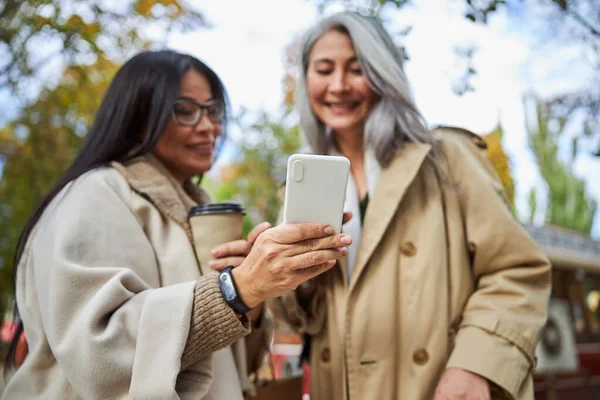 Радостные подруги используют смартфон на улице — стоковое фото