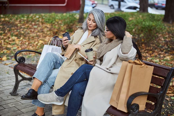 Kahve fincanları olan iki güzel kadın dışarıda bankta oturuyor.