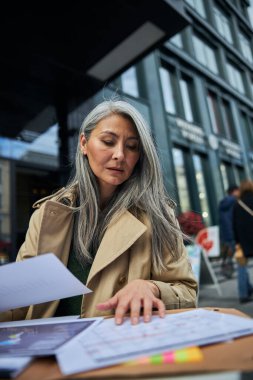 Açık kafede belgelerle çalışan ciddi bir iş kadını.