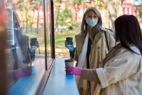 Elegantes mujeres en máscaras médicas bebiendo café y charlando al aire libre —  Fotos de Stock