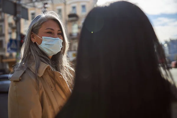 Encantadora mujer en máscara médica hablando con un amigo al aire libre —  Fotos de Stock