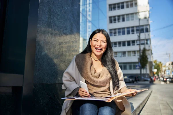 一个快乐的女人，带着手机和文件坐在外面的台阶上 — 图库照片