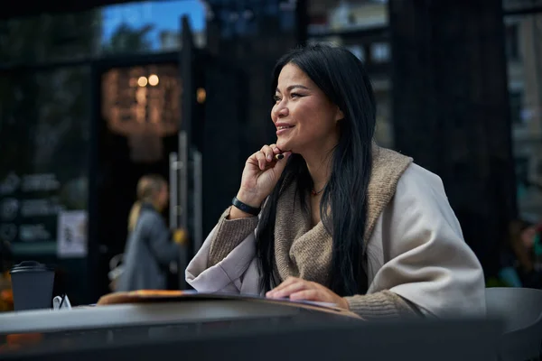 Красивая радостная женщина сидит за столом в кафе на открытом воздухе — стоковое фото