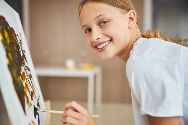 Chica rubia alegre pintando en el caballete — Foto de Stock