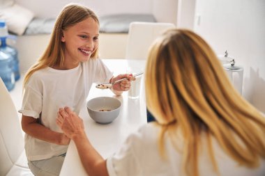 Neşeli kız kahvaltıda annesiyle konuşuyor.