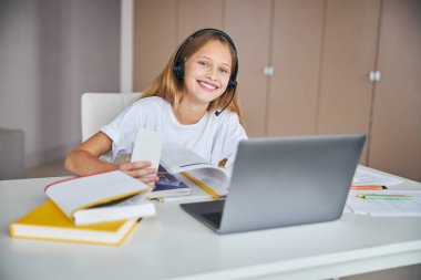 Dizüstü bilgisayarın karşısında cep telefonu olan bir kız öğrenci.