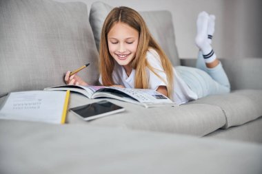 Yüzüstü uzanmış kitaba bakan bir kız.