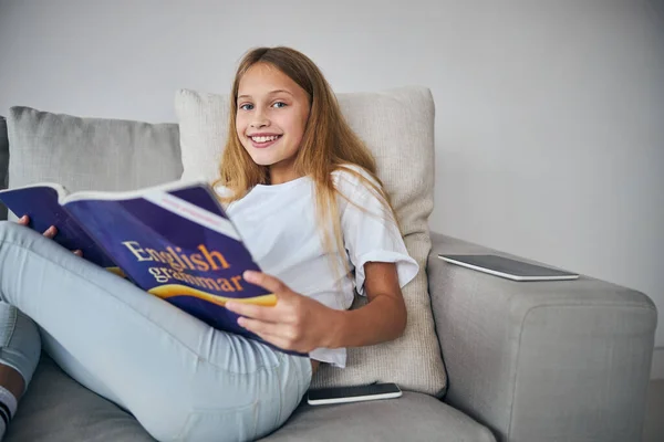 Mujer acostada en un sofá con un libro y gadgets —  Fotos de Stock