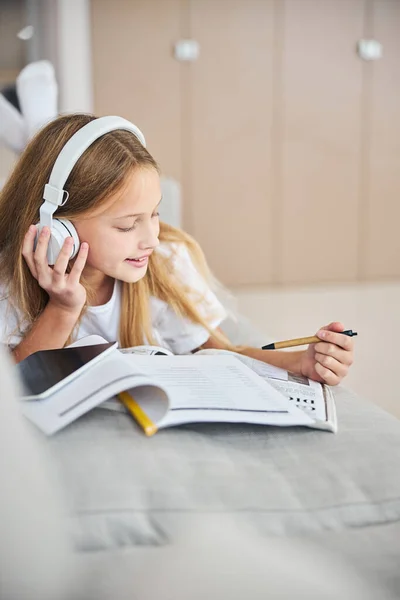 Minderjarige student geniet van de muziek tijdens een werk met woordenboek — Stockfoto