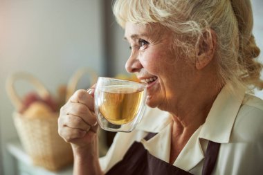 Neşeli yaşlı kadın evde taze çay içiyor.
