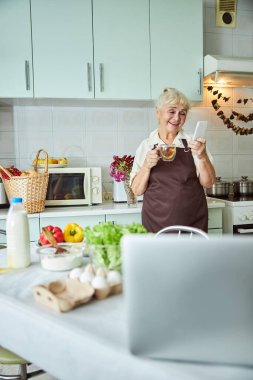 Mutfakta cep telefonu kullanan neşeli yaşlı kadın.