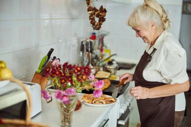 Mutfak tezgahında elinde turtayla neşeli yaşlı kadın.
