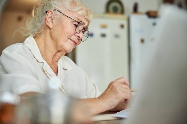 Güzel yaşlı kadın evde evrak çalışıyor.