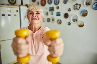 Keyifli yaşlı kadın evde dambıllarla egzersiz yapıyor.