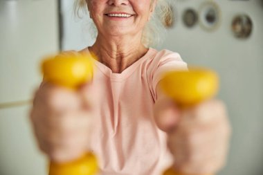Neşeli yaşlı kadın evde halterlerle egzersiz yapıyor.
