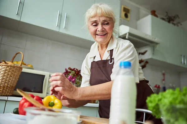 Веселая старушка в фартуке готовит ужин дома — стоковое фото