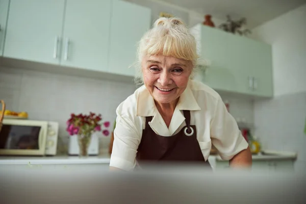 Милая старушка в фартуке, стоящая на кухне — стоковое фото