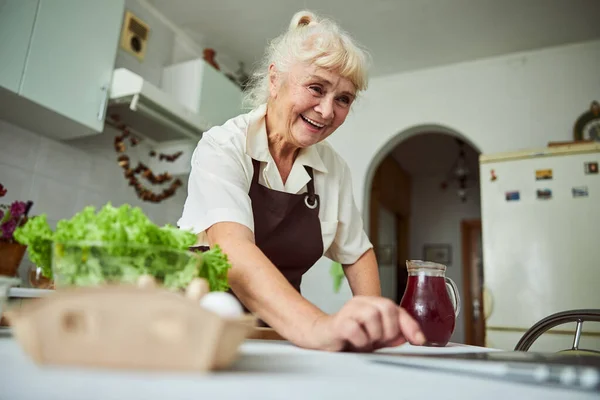 Веселая пожилая женщина, использующая ноутбук на кухне — стоковое фото