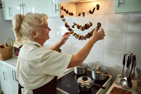 Mulher sênior agradável verificando cogumelos secos na cozinha — Fotografia de Stock