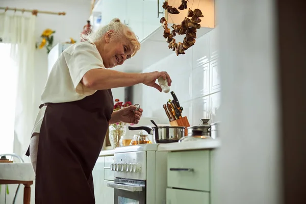 Joyful mulher idosa em avental cozinhar jantar na cozinha — Fotografia de Stock