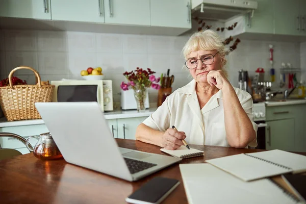 Evde dizüstü bilgisayarda çalışan hoşnutsuz yaşlı kadın.
