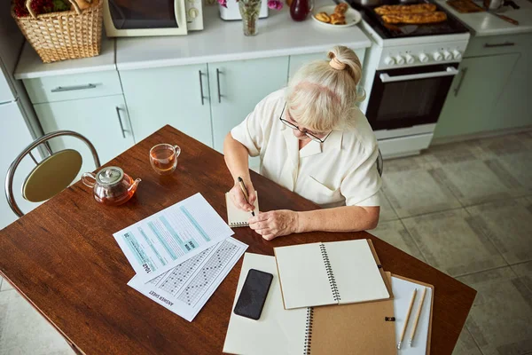 Vieille femme écrit sur carnet spirale à la maison — Photo