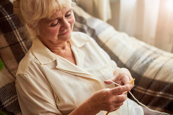 Koltuğunda oturmuş örgü ören sevimli yaşlı kadın.