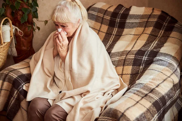 Chora staruszka dmucha nos w chusteczkę w domu — Zdjęcie stockowe