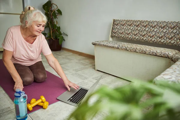 Laptop kullanan ve evde yoga yapan hoş bir yaşlı kadın.