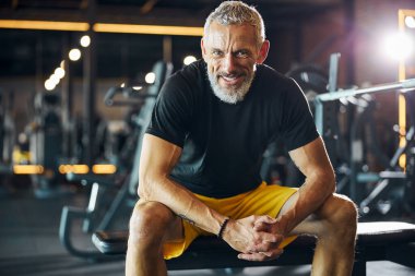 Mutlu bir gülümsemesi olan sporcu ağırlık bankında oturuyor.