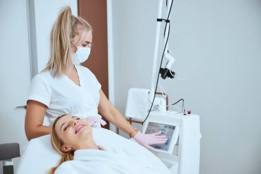 Dermatolog bir güzellik makinesinin ekranına dokunuyor.