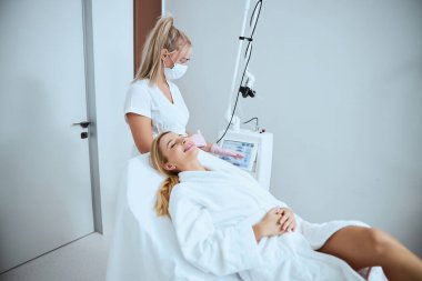 Kozmetik uzmanı gülümseyen hastasını güzellik prosedürüne hazırlıyor.