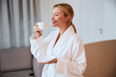 Gülümseyen spa müşterisi elinde bir fincan kokulu içecek tutuyor.