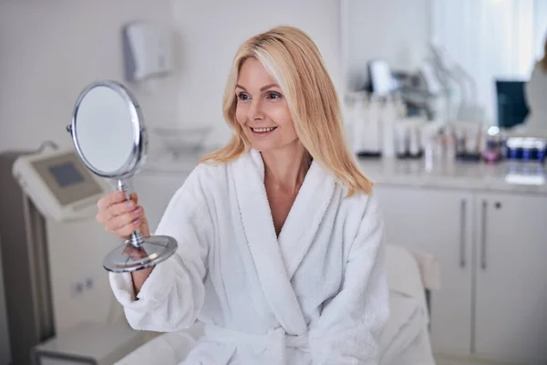 Красивая белая женщина с ручным зеркалом в руке в салоне красоты — стоковое фото