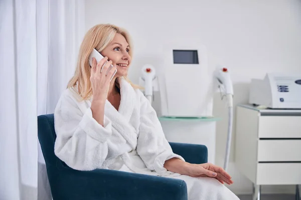 Прекрасна усміхнена кавказька самиця у білій халаті розмовляє по мобільному телефону в салоні краси. — стокове фото