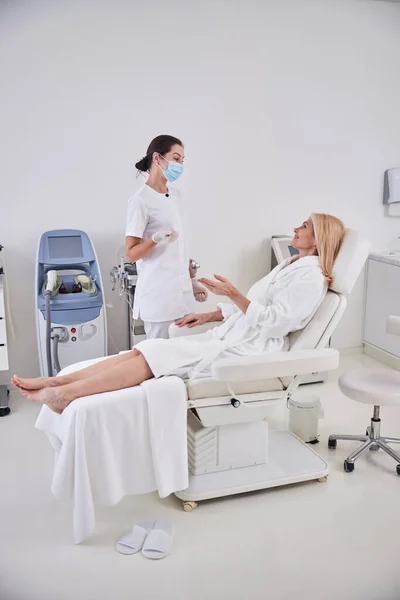 Good looking two women in white clothes talking together about spa treatment — Stock Photo, Image