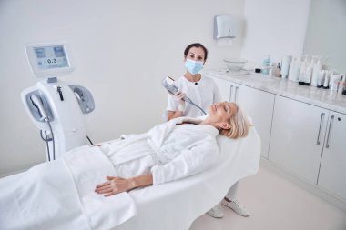 Professional female doctor working with patient while applying special ultrasound machine clipart