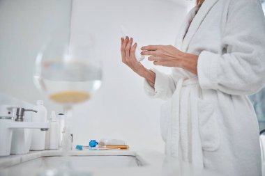 Yetişkin, zarif bir kadın, kollarında bir şişeyle bir şeyler okuyor.