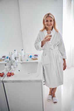 Kameraya bakarken elinde su olan güzel bir bayan bardak tutuyor.