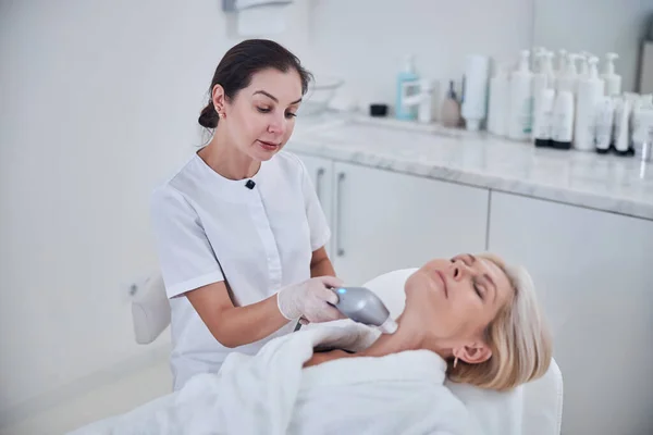 Female dermatologist using new special cosmetology device for skin care of beautiful patient of beauty clinic — Stock Photo, Image