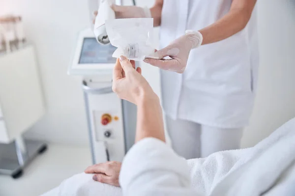 Frau hält Medikamentenpräparat in der Hand, während sie mit Arzt in kosmetologischer Klinik spricht — Stockfoto