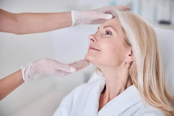 Attraente signora sorridente seduta sul divano di bellezza e guardando il medico in clinica di bellezza — Foto Stock