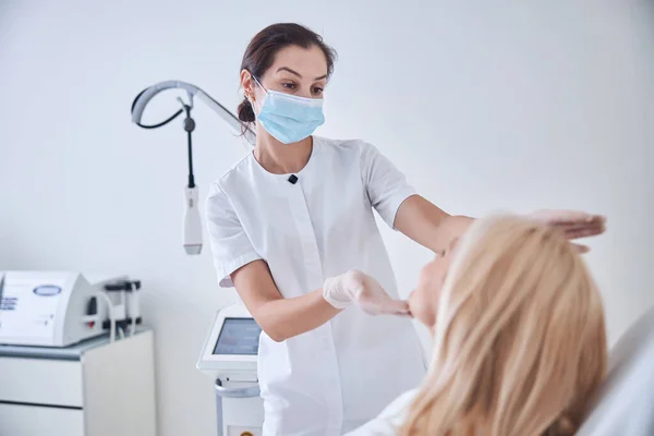 Beautiful brunette doctor examining skin on female face in beauty cabinet — Stock Photo, Image