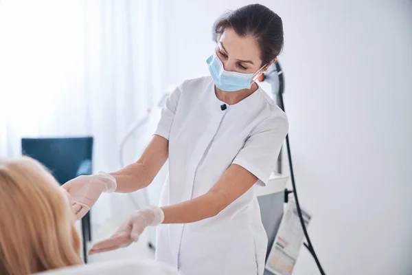 Vážně kosmetička v bílém oblečení mluví s blondýnou v moderní kosmetické klinice — Stock fotografie