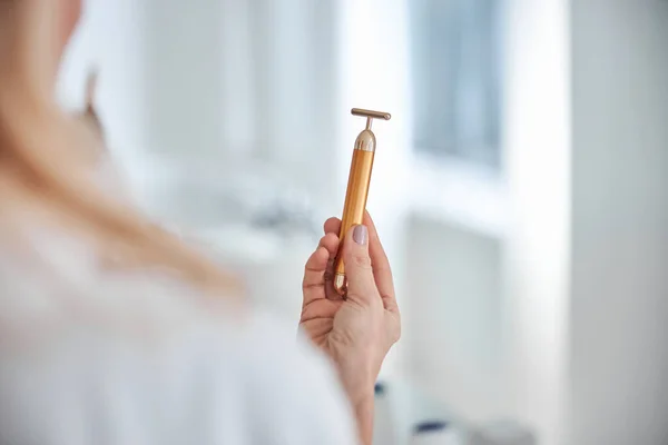 Bela mulher segurando massageador no braço no banheiro — Fotografia de Stock