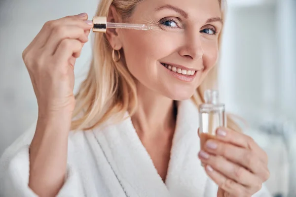 Aceite cosmético que aplica en la cara de la mujer joven —  Fotos de Stock
