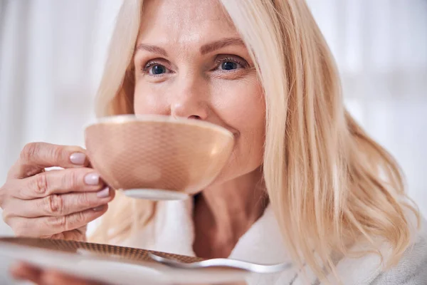 Feliz mujer alegre sosteniendo la taza de té en la mano en la habitación dentro —  Fotos de Stock